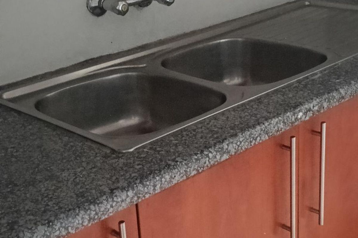 A functional kitchen area featuring a double bowl stainless steel sink, granite countertops, and wood-finish cabinetry with modern metal handles.