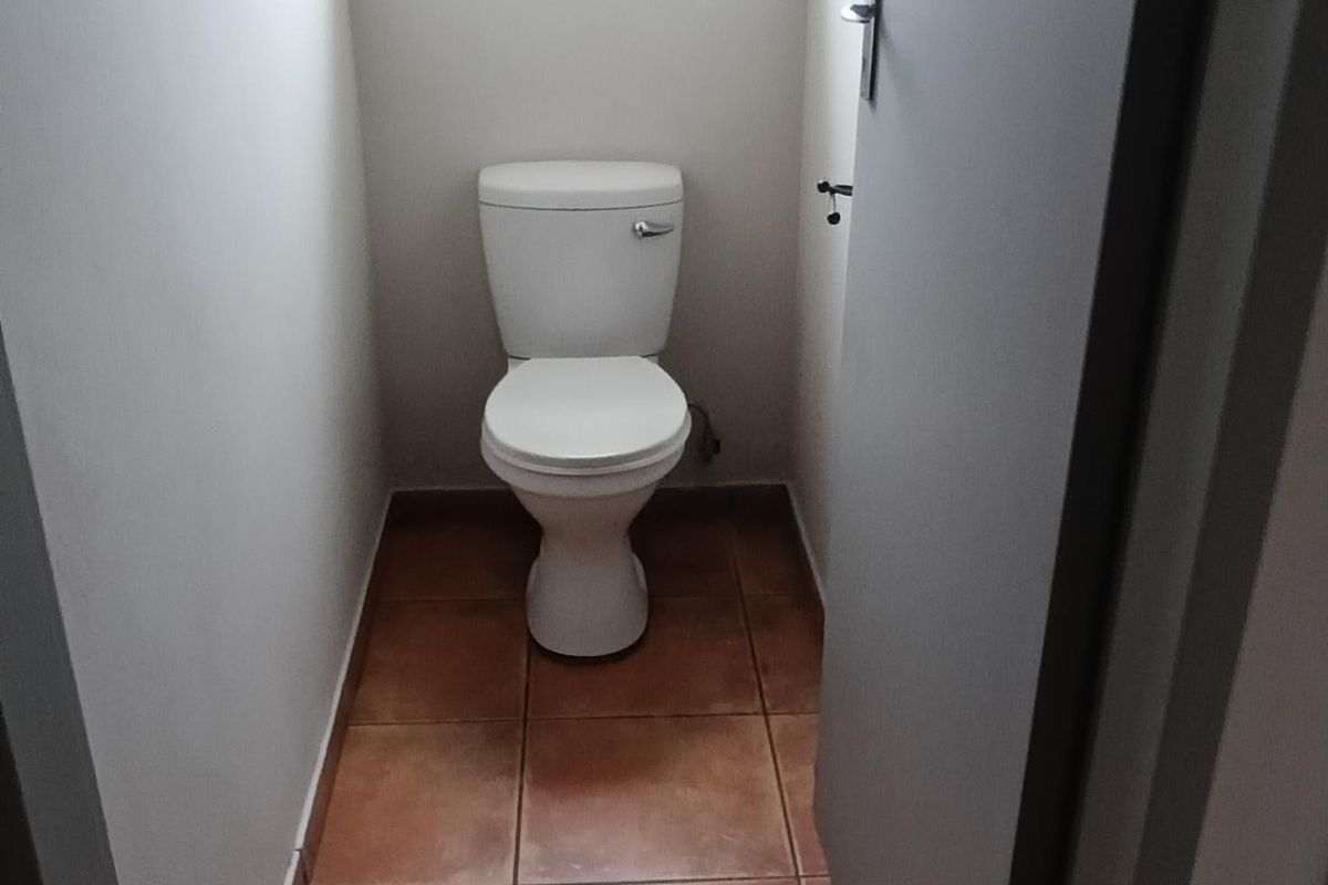A compact, functional restroom featuring tiled flooring, a standard toilet, and a small window for natural light.