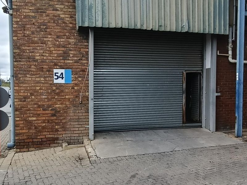 Industrial unit exterior featuring a brick facade, metal cladding, and a large roller shutter door with a separate pedestrian entrance.