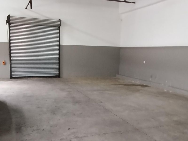 Spacious industrial utility area featuring high exposed steel roof trusses, concrete flooring, and a secure roller shutter door.