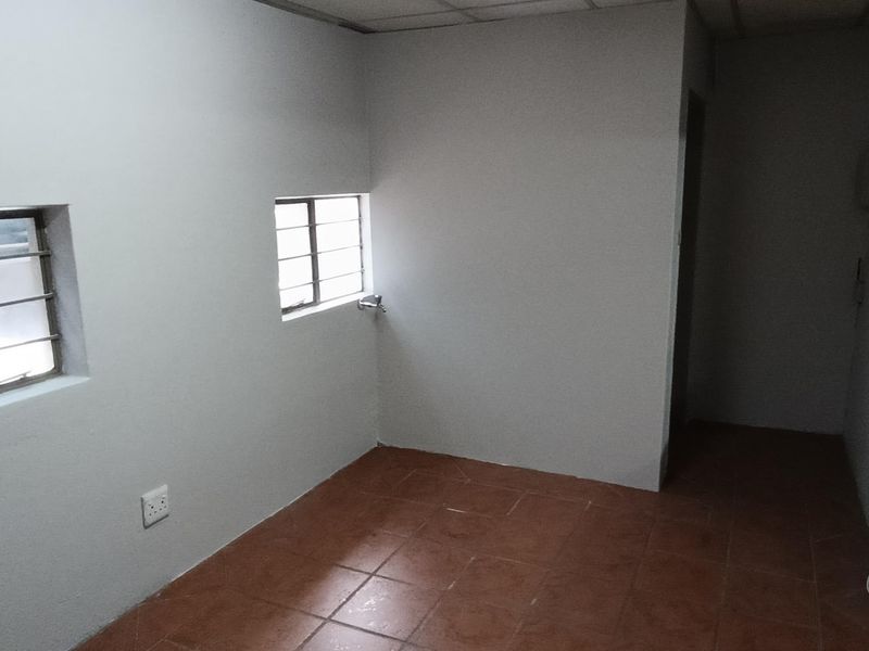 A vacant industrial office space featuring tiled flooring, security bars on windows, and a drop ceiling, providing a functional and clean work environment.