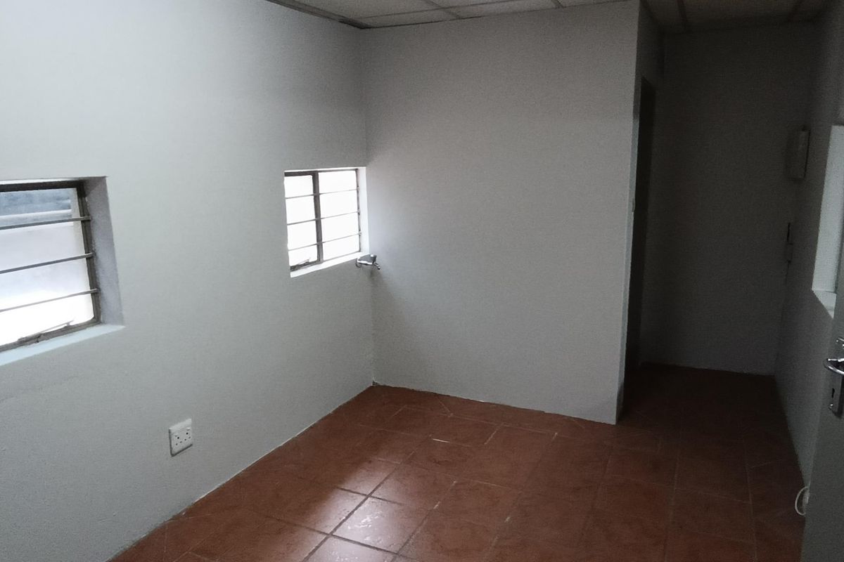 A vacant industrial office space featuring tiled flooring, security bars on windows, and a drop ceiling, providing a functional and clean work environment.
