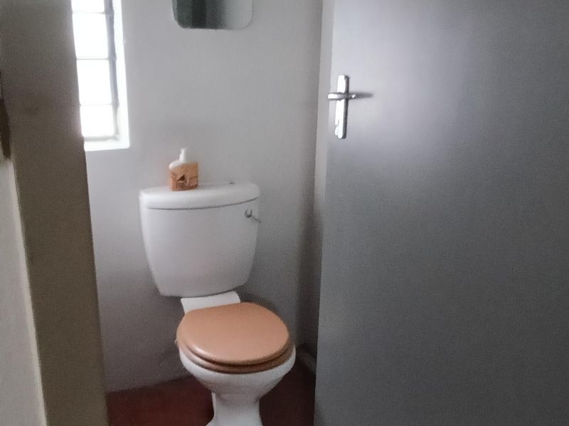 A compact bathroom featuring a standard toilet, tiled flooring, and a window, providing essential utility space.
