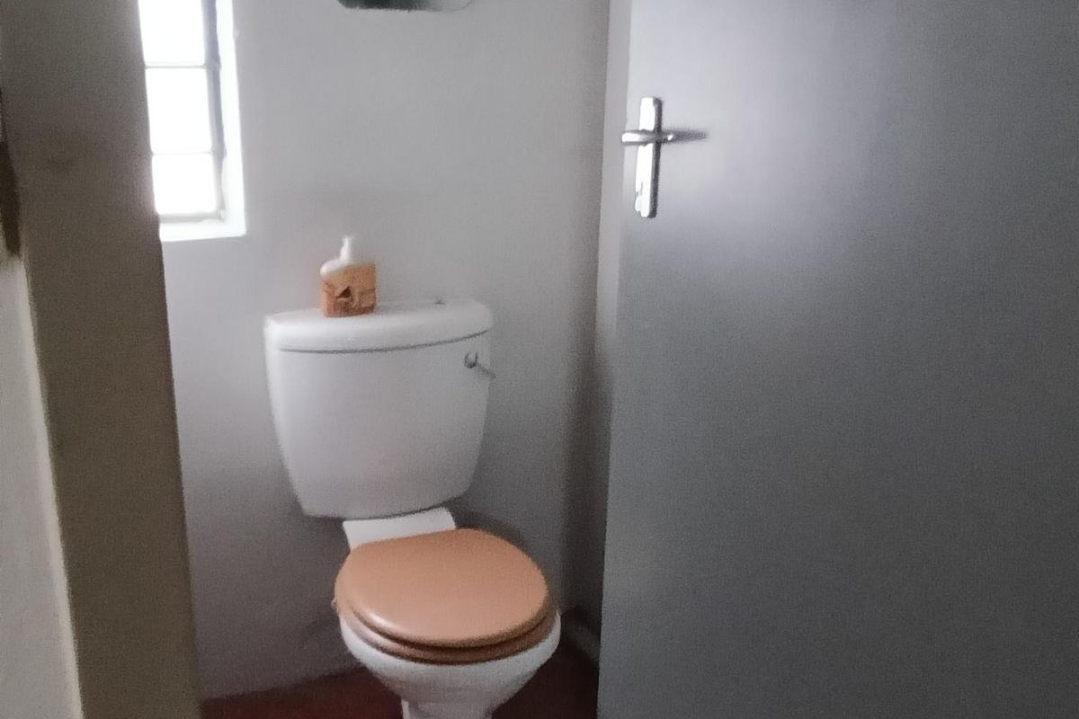 A compact bathroom featuring a standard toilet, tiled flooring, and a window, providing essential utility space.