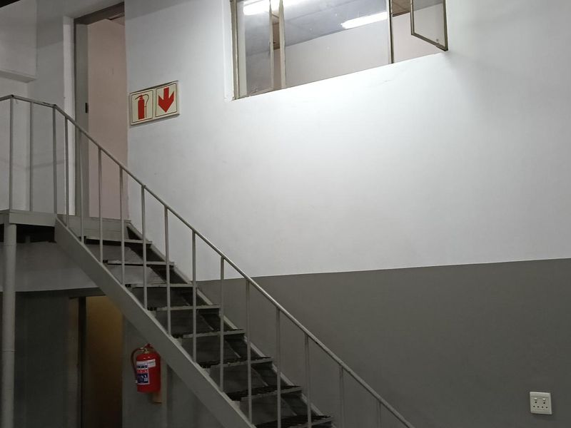 Industrial utility space featuring a metal staircase leading to a mezzanine level, with high ceilings and functional fire safety equipment.