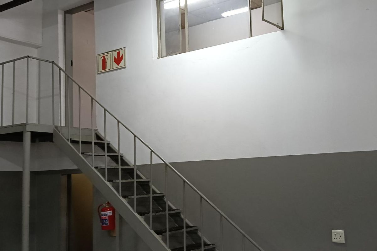 Industrial utility space featuring a metal staircase leading to a mezzanine level, with high ceilings and functional fire safety equipment.