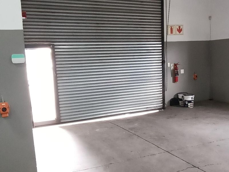 Industrial garage space featuring a large roller shutter door, exposed steel roof trusses, and durable concrete flooring with minor surface cracking.