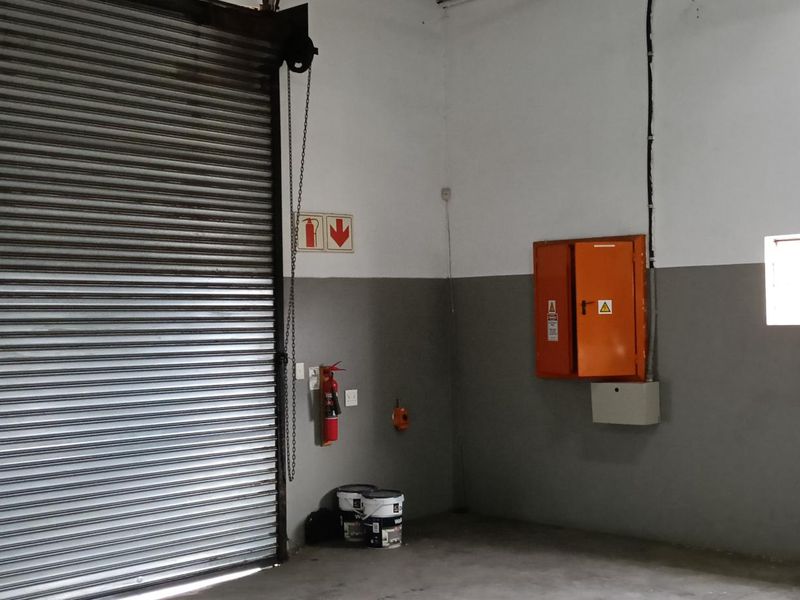Industrial garage space featuring a large roller shutter door, concrete flooring, and wall-mounted electrical distribution board.
