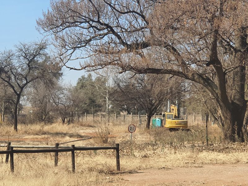 A view of the vacant commercial land featuring mature trees, perimeter fencing, and an unpaved access road.