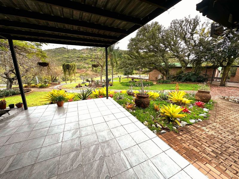 A spacious covered patio featuring modern tiled flooring, overlooking a well-maintained garden with mature trees and scenic landscape views.