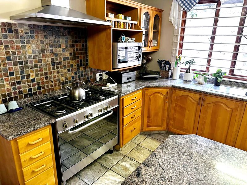 A functional kitchen featuring wooden cabinetry, granite countertops, a gas stove with extractor fan, and a mosaic tile backsplash.