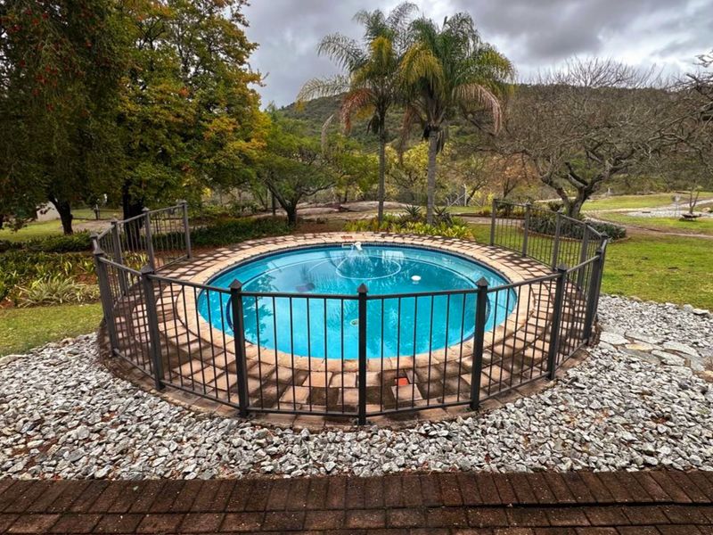 A circular swimming pool featuring a metal safety fence, surrounded by stone landscaping and brick paving in a garden setting.