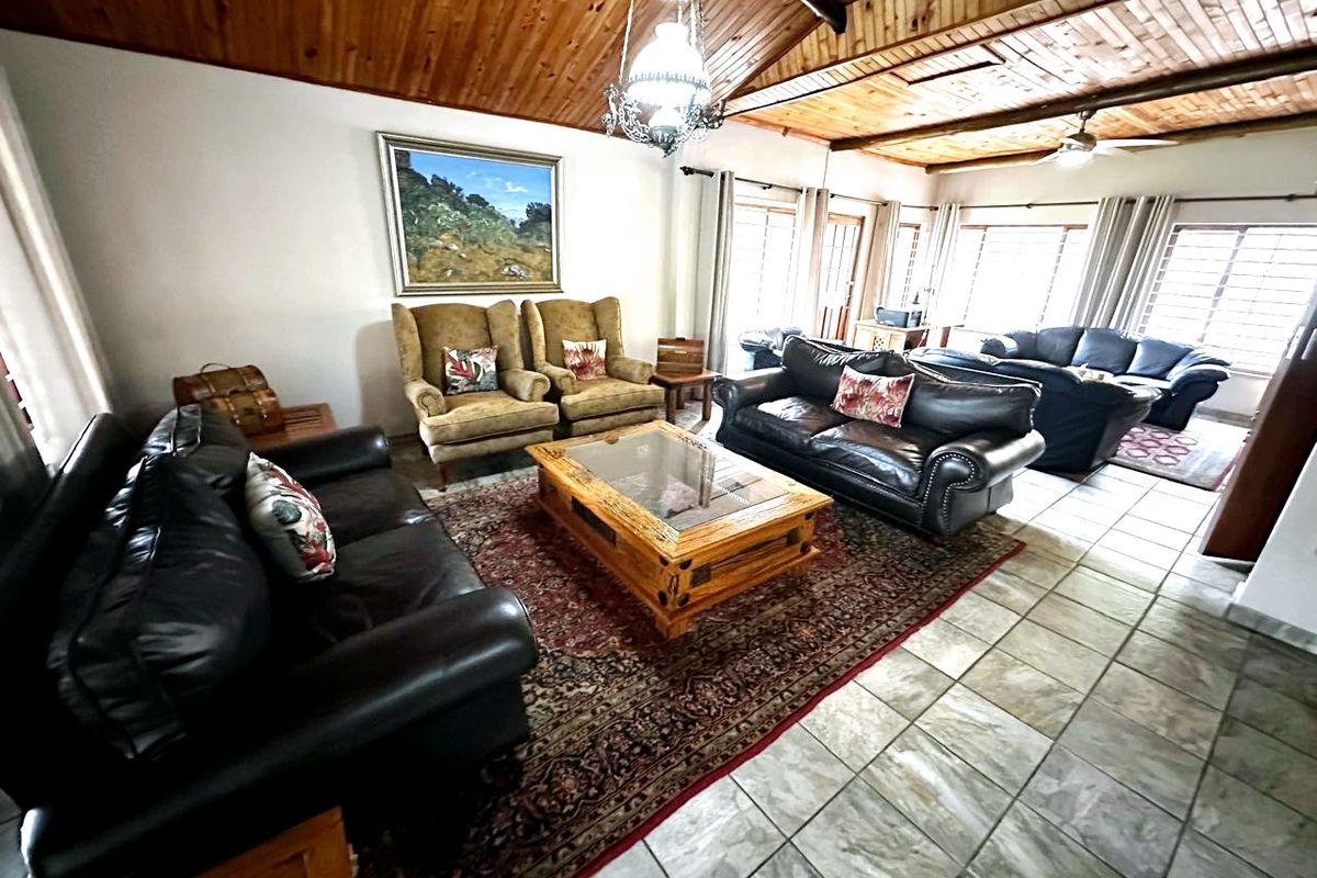 Spacious living room featuring a high exposed timber beam ceiling, tiled flooring, and large windows providing ample natural light.