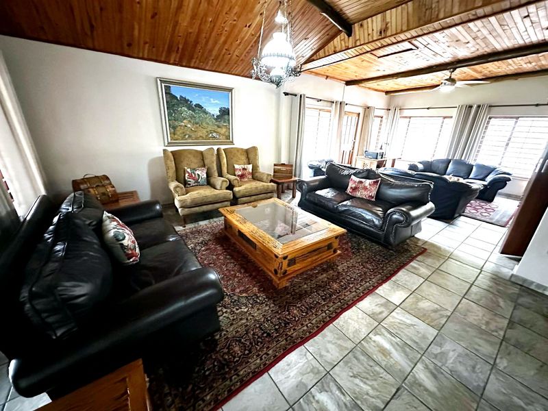 Spacious living room featuring a high exposed timber beam ceiling, tiled flooring, and large windows providing ample natural light.