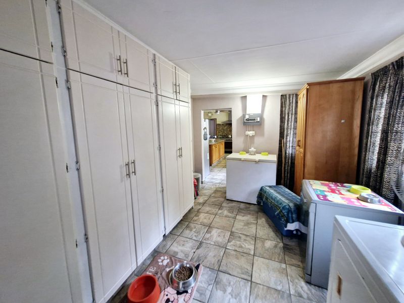 A functional laundry area featuring extensive built-in cabinetry for storage and durable tiled flooring, with a convenient layout leading into the kitchen.