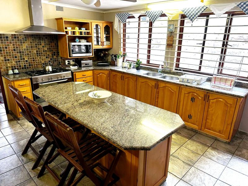 Spacious kitchen featuring granite countertops, wooden cabinetry, a central island, and a gas hob with a stainless steel extractor fan.