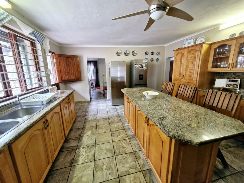 Spacious kitchen featuring granite countertops, wooden cabinetry, a central island, and tiled flooring, offering a functional layout with ample storage space.