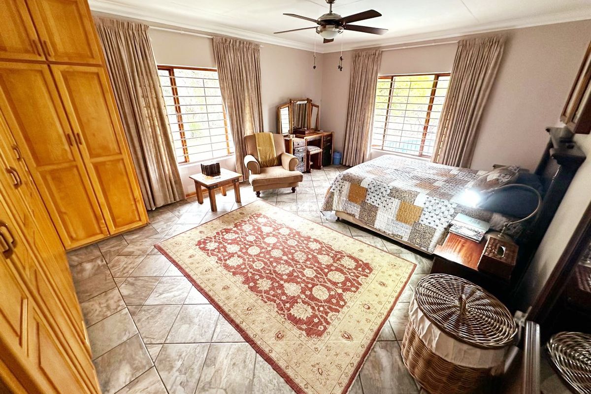Spacious bedroom featuring tiled flooring, built-in wooden cupboards, and large windows with security bars, offering a functional and well-lit living space.