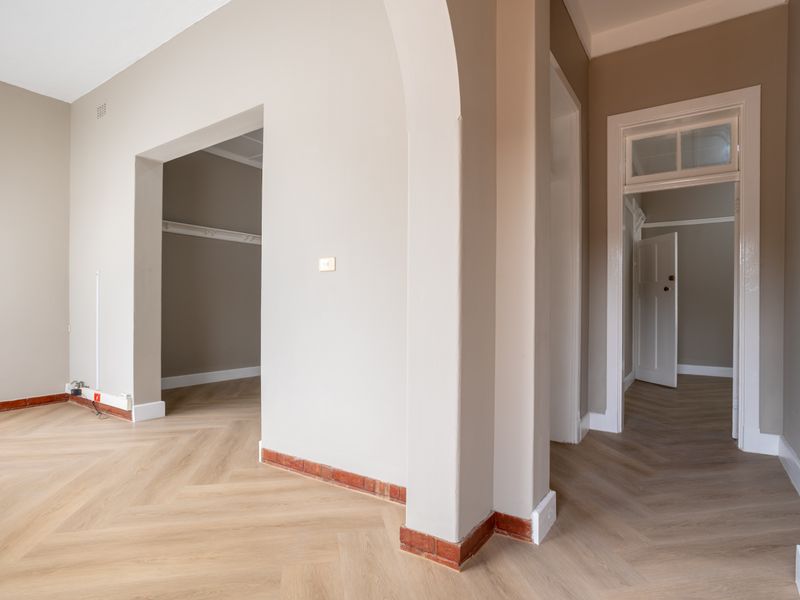 A bright, vacant office space featuring elegant herringbone timber flooring, an arched architectural transition, and classic interior door frames with transom windows.