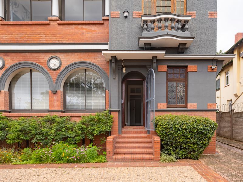 A well-maintained historic office building facade featuring classic red brickwork, arched windows, a decorative balcony, and a welcoming brick-stepped entrance.