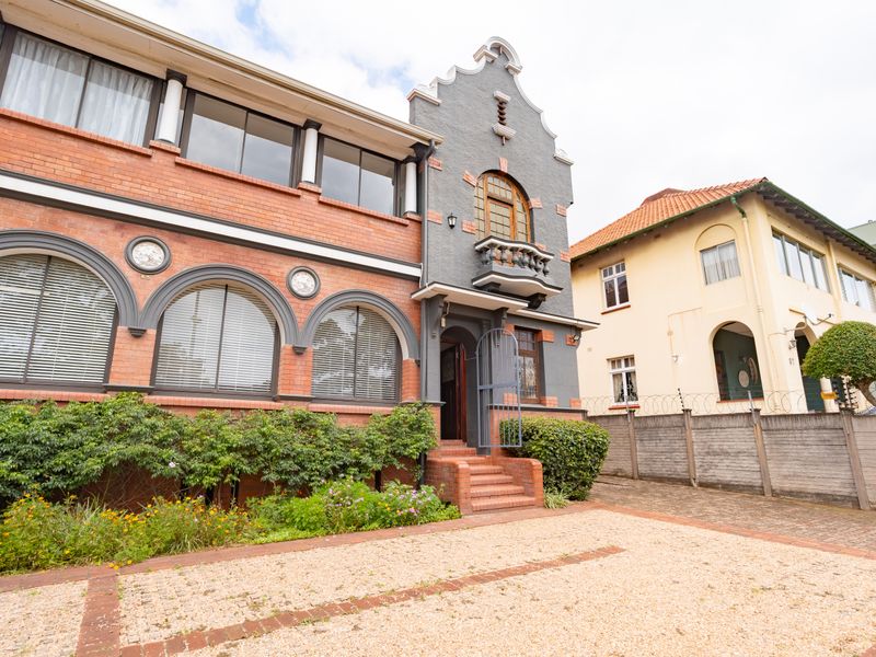 A well-maintained office building featuring classic brick architecture, arched windows, a small balcony, and a gravel driveway with secure perimeter fencing.