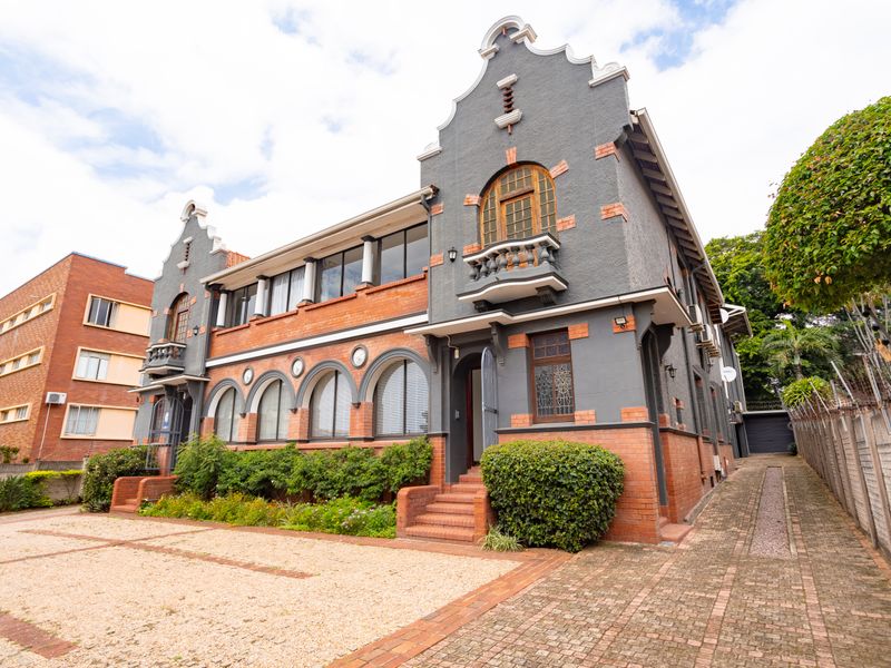 A well-maintained historic-style office building featuring a brick and rendered facade, arched windows, and a paved driveway with ample parking space.