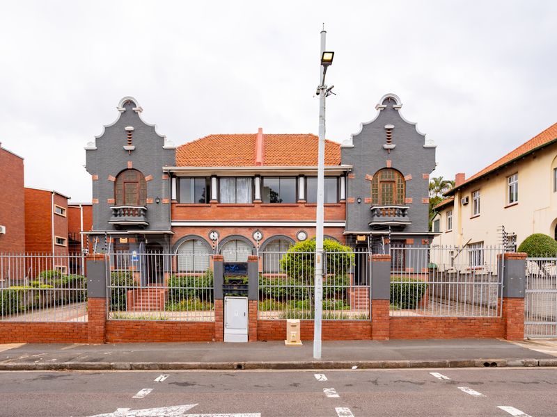 A well-maintained historic office building featuring a brick facade, terracotta roof tiles, arched windows, and secure perimeter fencing with gated access.
