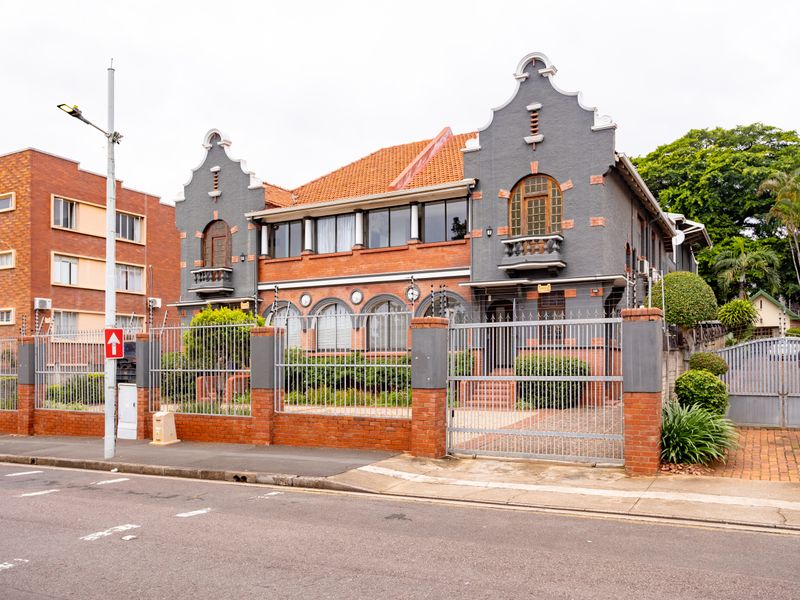 A well-maintained historic-style office building featuring a brick and rendered facade, arched windows, balconies, and secure perimeter fencing with gated access.