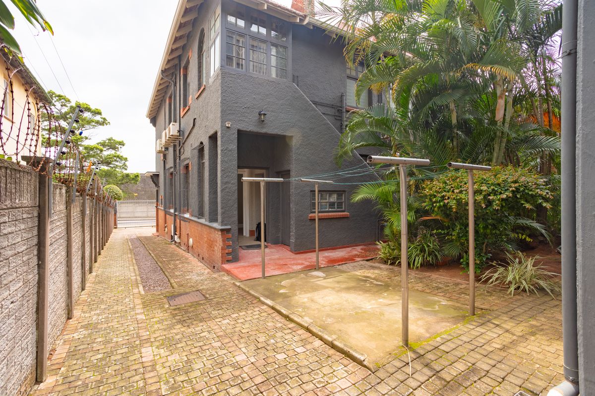 Rear exterior view of the office property featuring a paved driveway, secure boundary wall with razor wire, and an outdoor concrete utility area.