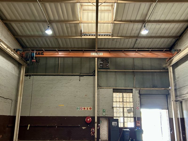 Spacious industrial warehouse unit featuring high ceilings, an integrated overhead crane, natural skylight illumination, and a large roller shutter door for easy access.