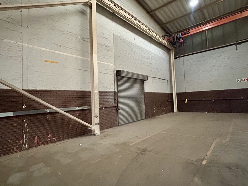 Spacious industrial warehouse unit featuring high ceilings, an overhead crane, concrete flooring, and a secure roller shutter door for easy access.
