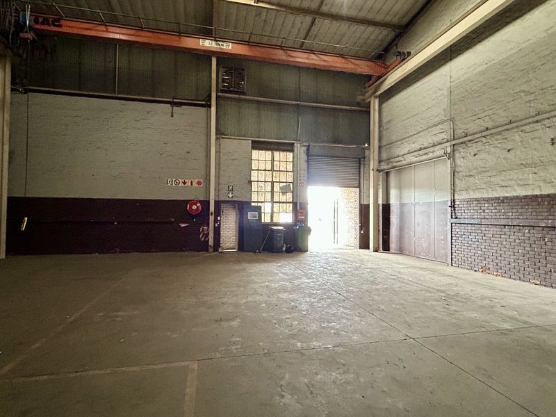Spacious industrial warehouse unit featuring high ceilings, an overhead crane, concrete flooring, and a large roller shutter door for easy access.