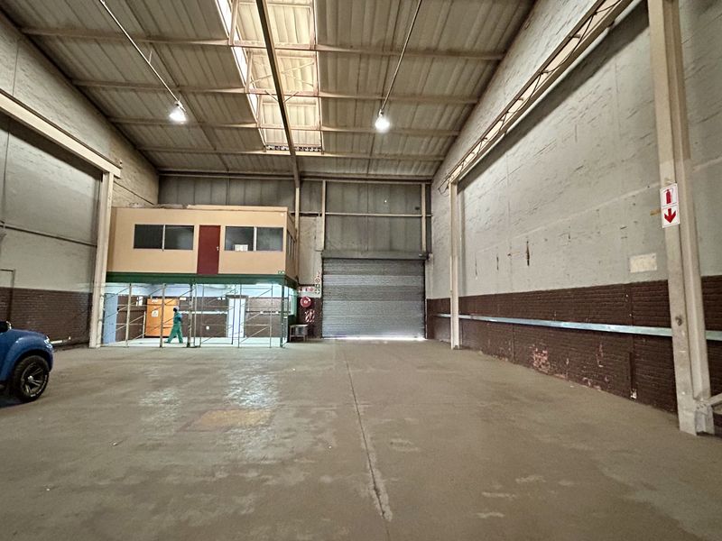 Spacious industrial warehouse featuring high ceilings, exposed steel trusses, a roller shutter door, and an integrated mezzanine office area.