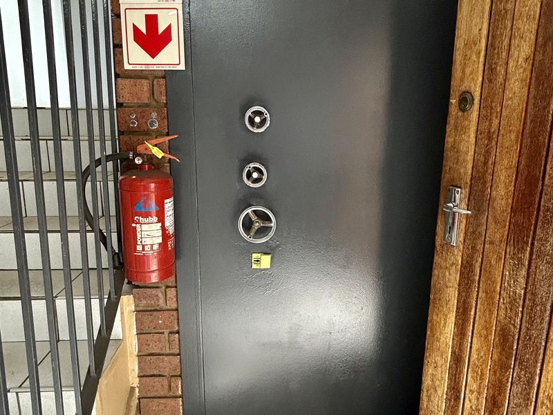 A secure utility area featuring a heavy-duty steel vault door, tiled flooring, and a wall-mounted fire extinguisher adjacent to a staircase.