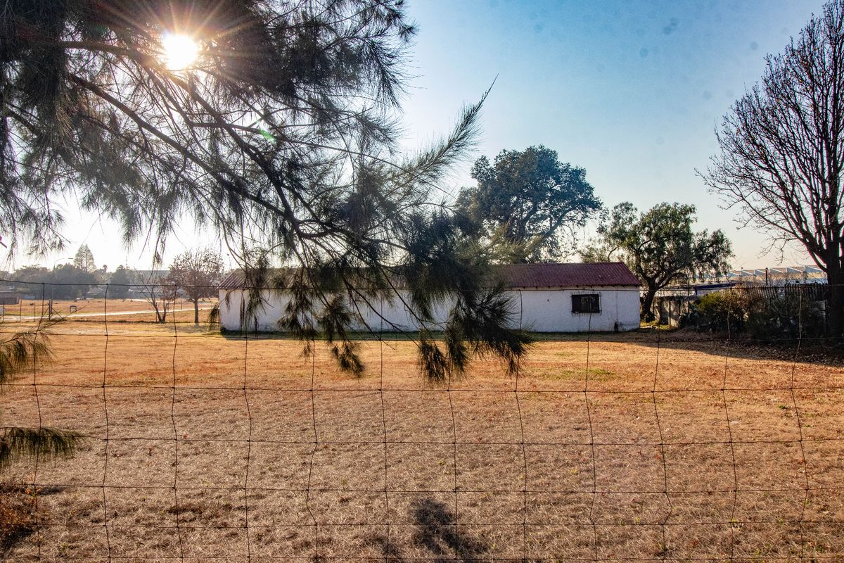 A view of a detached commercial building structure set back on a large plot of land, enclosed by a wire mesh fence.