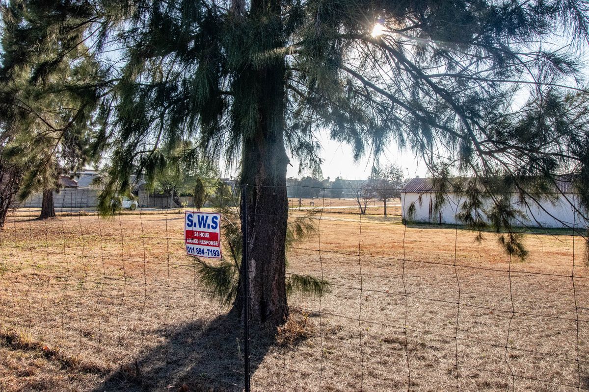 A view of a large, open commercial plot featuring wire mesh perimeter fencing and a small outbuilding structure.