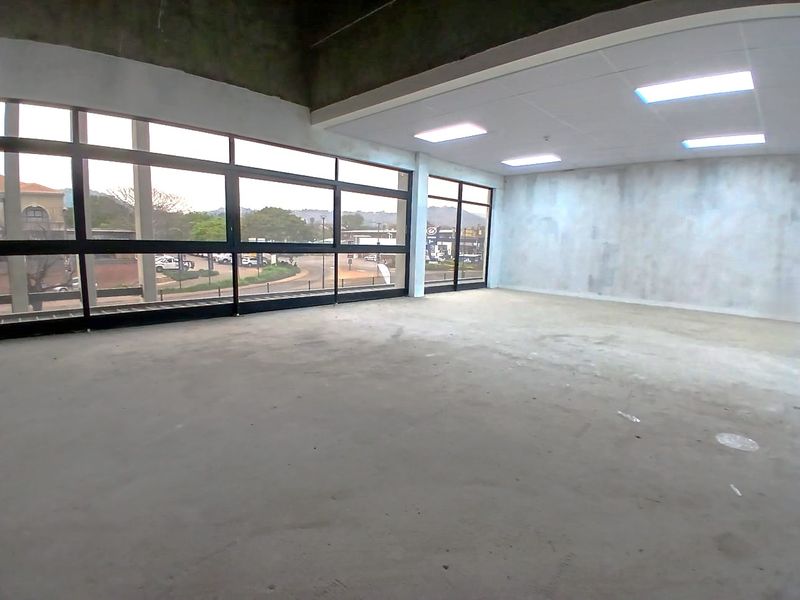 A spacious, open-plan office area featuring large windows, concrete flooring, and a suspended ceiling, currently in an unfinished shell condition.