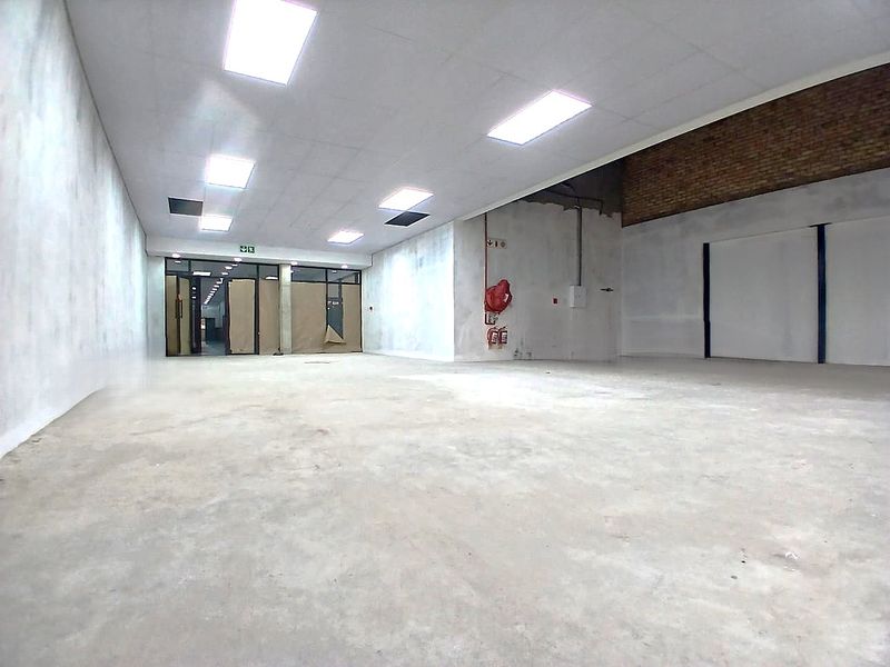 A spacious, open-plan office area featuring concrete floors, suspended ceilings with recessed lighting, and an exposed brick feature wall, currently in shell condition.
