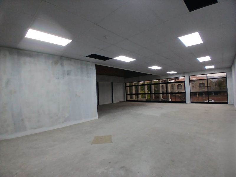 An open-plan office space featuring large windows, recessed lighting, and a suspended ceiling, currently in need of cosmetic refurbishment.