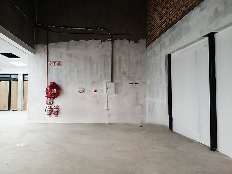 An unfinished office space featuring exposed brickwork, concrete flooring, and essential fire safety equipment including a hose reel and extinguishers.
