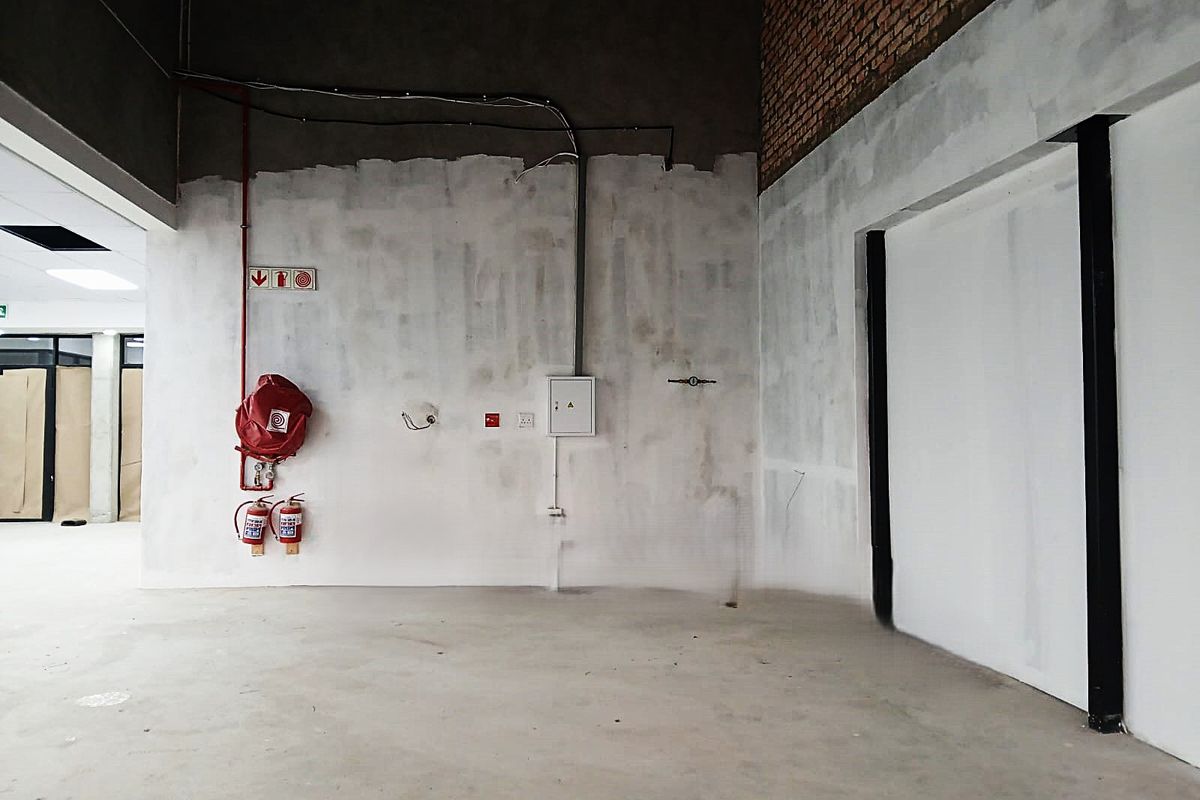 An unfinished office space featuring exposed brickwork, concrete flooring, and essential fire safety equipment including a hose reel and extinguishers.