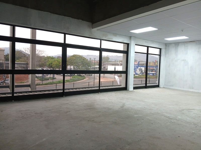 An open-plan office space in shell condition featuring large windows, suspended ceilings with recessed lighting, and concrete flooring, ready for custom fit-out.