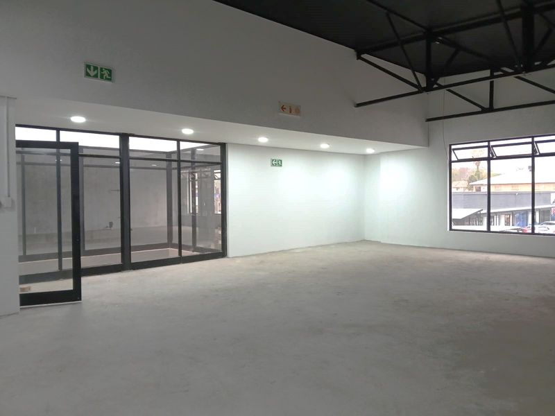 Spacious open-plan retail area featuring high ceilings with exposed steel trusses, modern glass partitioning, and ample natural light through large windows.