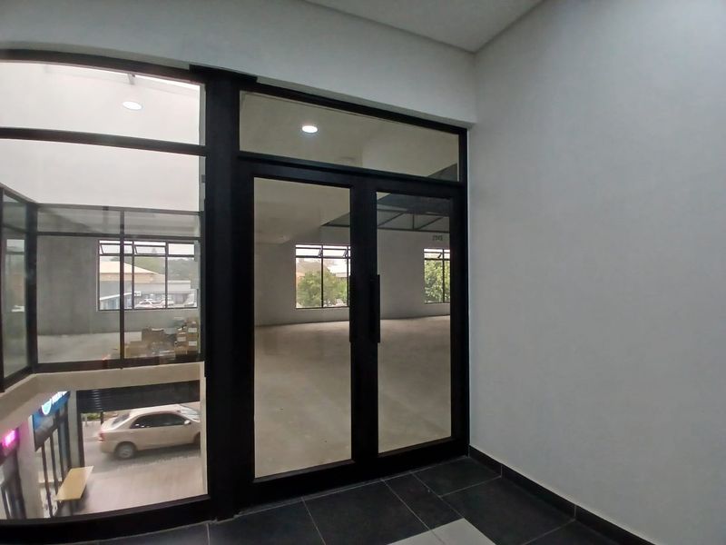A bright, modern commercial entry space featuring black aluminum-framed glass doors and large windows, providing an open and professional aesthetic for a retail unit.