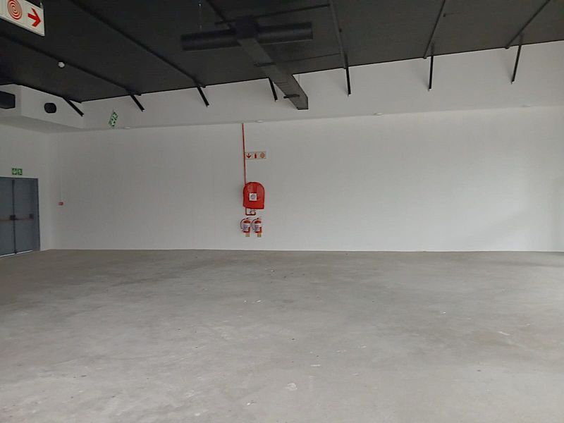A spacious, open-plan retail utility area featuring concrete flooring, an exposed ceiling, and essential fire safety equipment.
