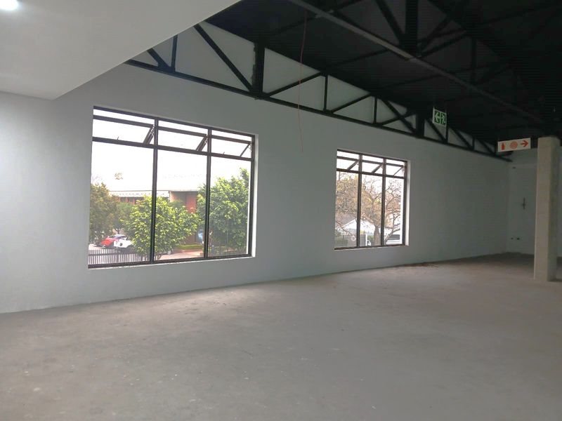 Spacious open-plan retail unit featuring high exposed steel roof trusses, large windows providing natural light, and polished concrete flooring.