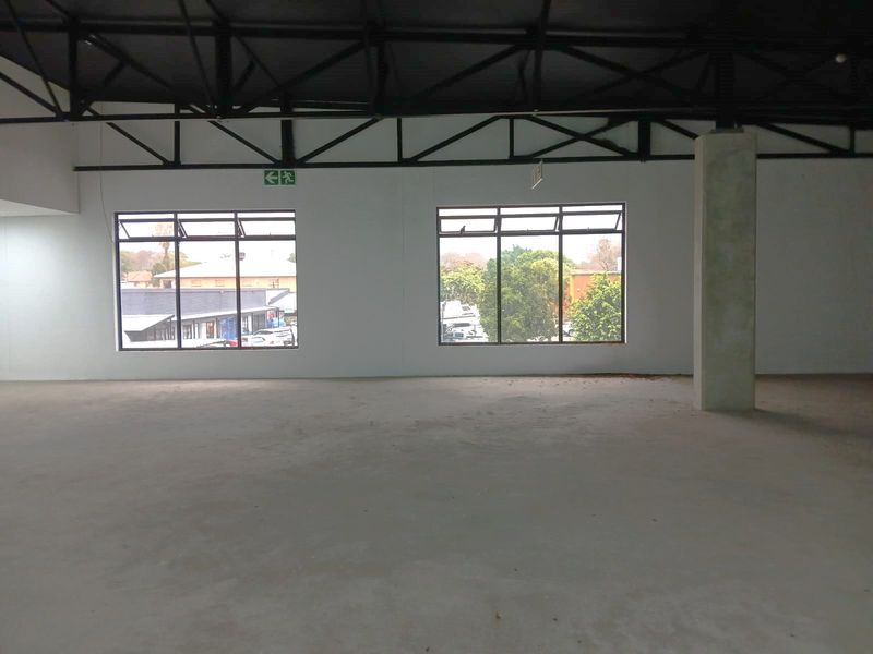 Spacious open-plan retail area featuring exposed steel roof trusses, large aluminium windows, and a concrete support column, offering a versatile blank canvas.
