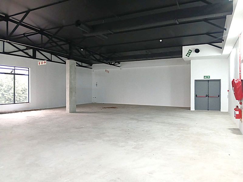 Spacious open-plan retail unit featuring exposed steel roof trusses, concrete flooring, and dedicated fire exit access.