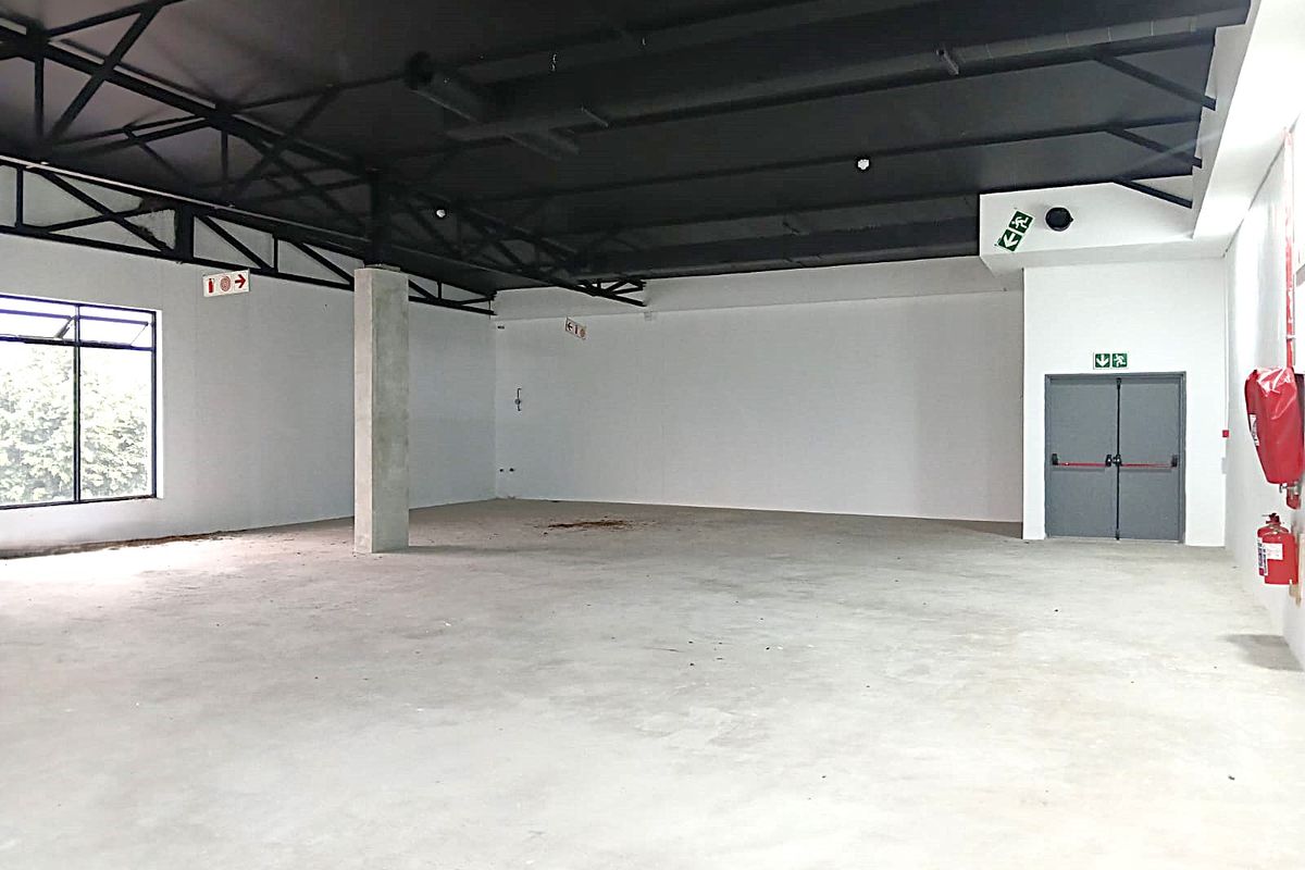 Spacious open-plan retail unit featuring exposed steel roof trusses, concrete flooring, and dedicated fire exit access.