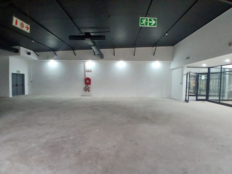 A spacious, open-plan retail unit featuring an exposed ceiling, polished concrete flooring, and integrated emergency safety fixtures, ready for custom fit-out.
